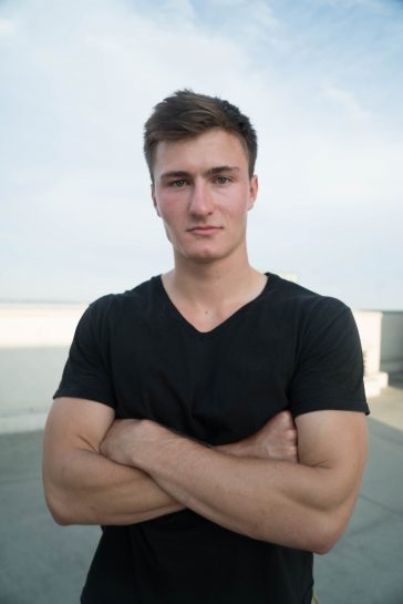 A photo of a man posing with his arms folded across his chest, looking muscly. 